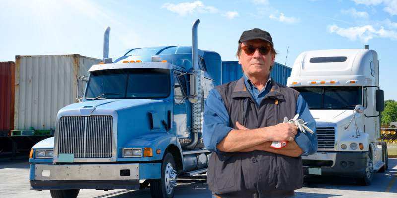 Owner Operator semi truck driver standing in front of heavy duty trucks.