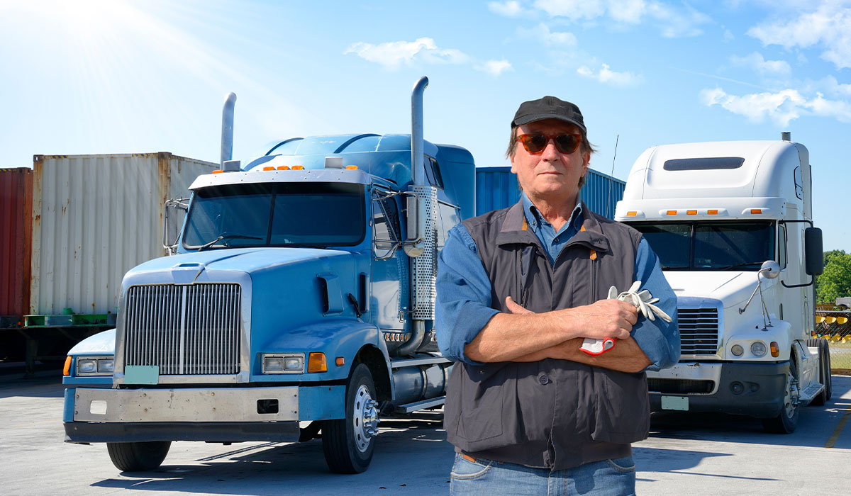 Owner Operator semi truck driver standing in front of heavy duty trucks.