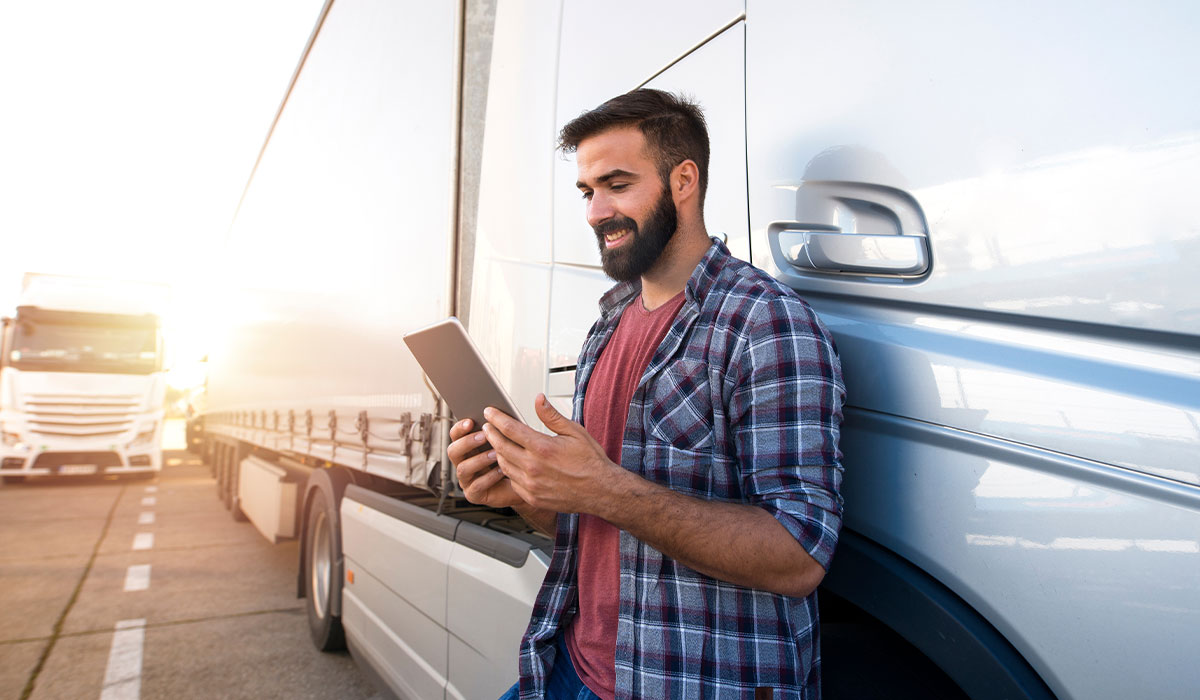 Man reviewing his tablet while leaning against a semi truck