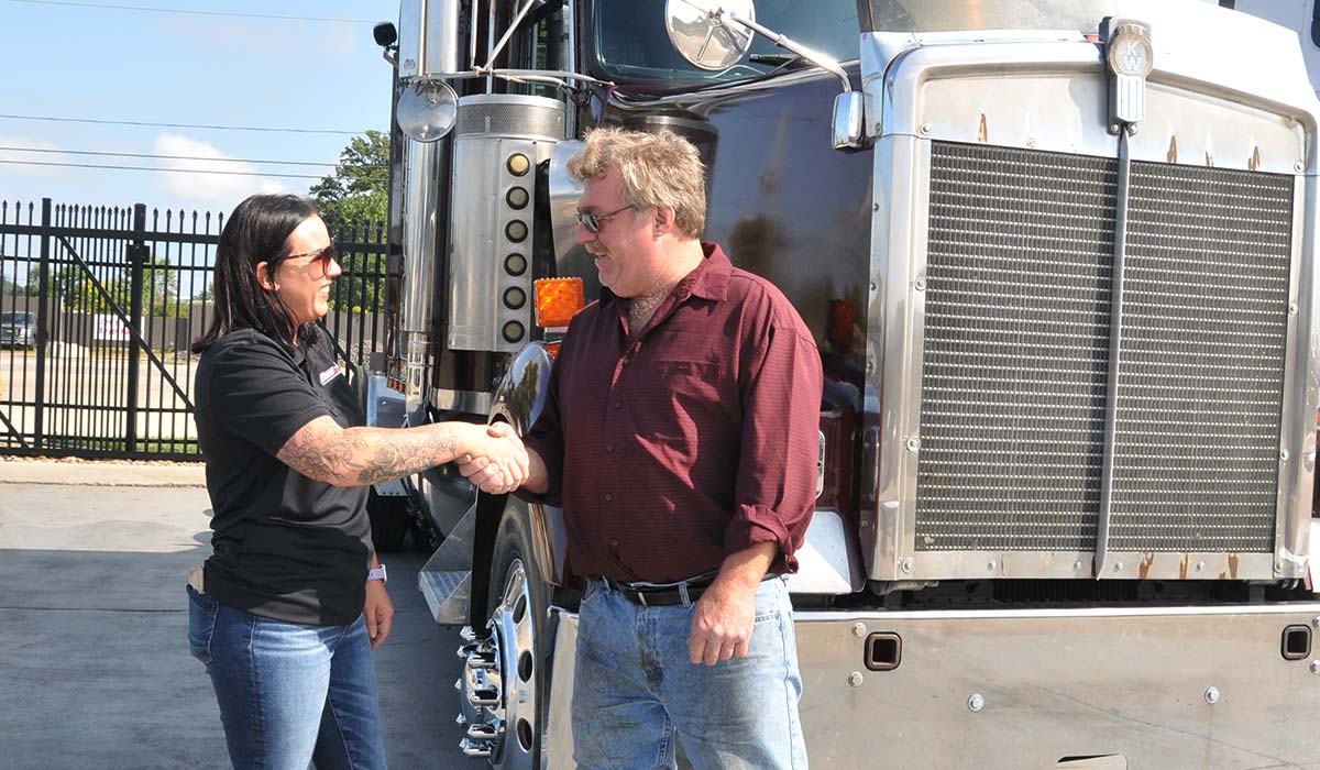 Salesperson shaking hands with a man who just bought a Kenworth semi truck