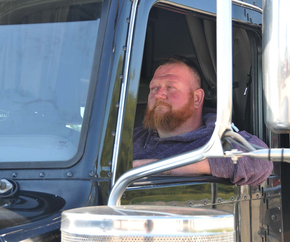 Man driving a semi truck with his elbow resting out the window.