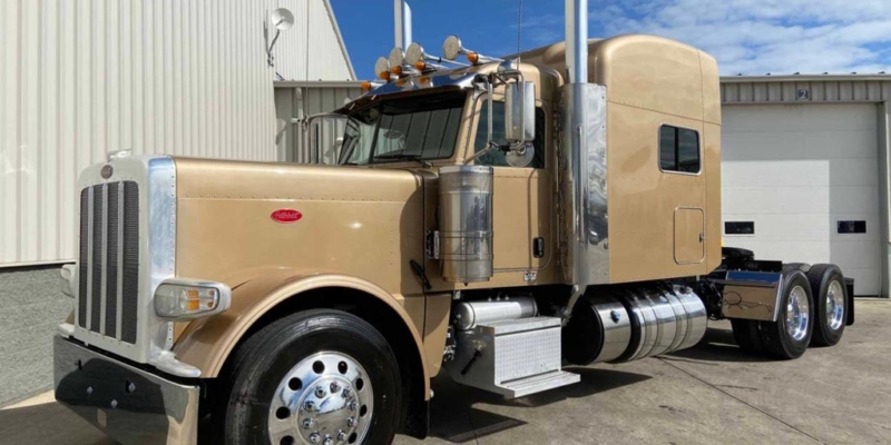 A tan peterbilt 389 semi truck parked in front of a building