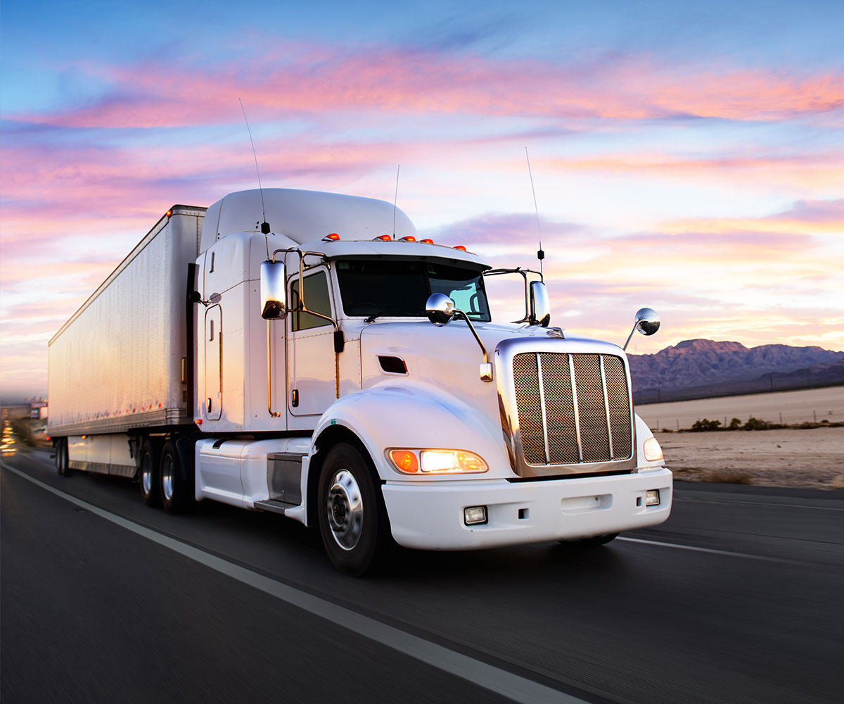 White semi truck driving down the highway with a sunset in the background